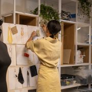 Designer organiza um painel de referências com croquis e amostras de tecidos em seu ateliê.