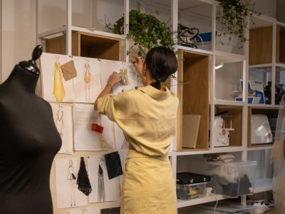 Designer organiza um painel de referências com croquis e amostras de tecidos em seu ateliê.