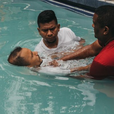 Três homens participam de uma cerimônia de batismo cristão em uma piscina
