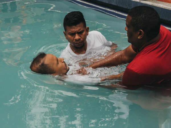 Três homens participam de uma cerimônia de batismo cristão em uma piscina