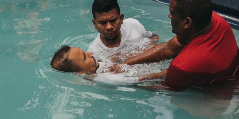 Três homens participam de uma cerimônia de batismo cristão em uma piscina