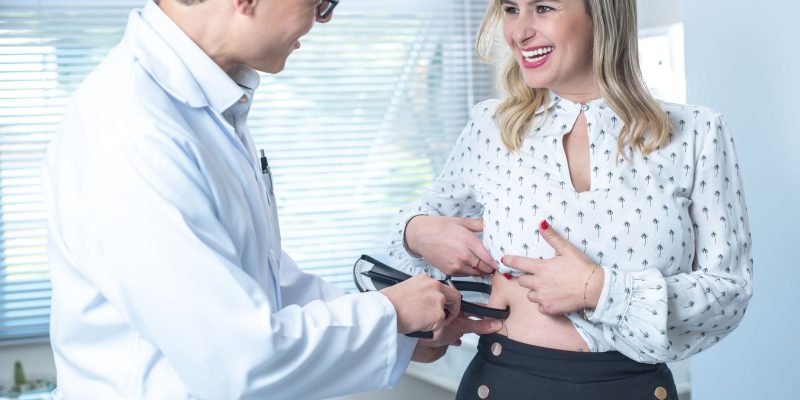Profissional de saúde mede a gordura corporal de uma paciente durante uma consulta clínica.