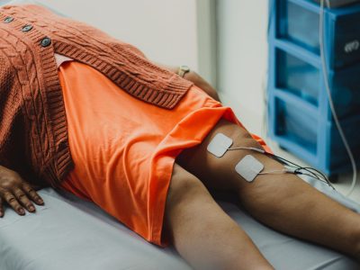 Close das pernas de uma mulher durante uma sessão de eletroterapia em ambiente hospitalar.