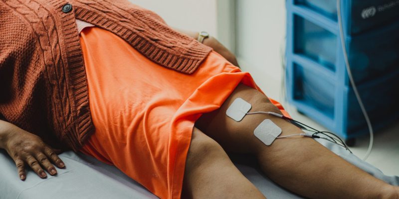 Close das pernas de uma mulher durante uma sessão de eletroterapia em ambiente hospitalar.