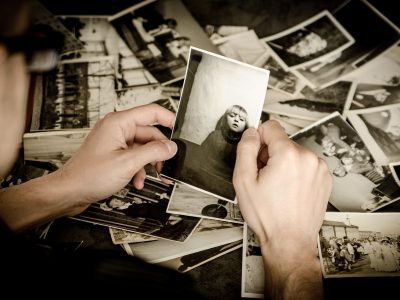 Mãos seguram fotografias antigas em preto e branco, evocando memórias e arquivo familiar.