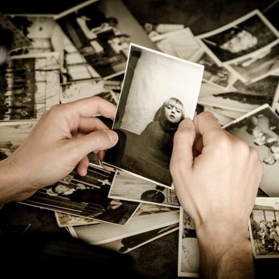 Mãos seguram fotografias antigas em preto e branco, evocando memórias e arquivo familiar.