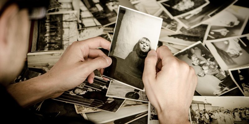 Mãos seguram fotografias antigas em preto e branco, evocando memórias e arquivo familiar.